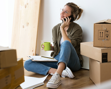 woman sitting on ground talking on phone with clipboard and boxes on the floor