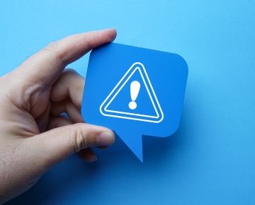 hand holding exclamation mark against blue background