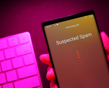 hand holding phone saying suspected spam over keyboard against pink background