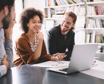 two male employees and one female employee looking at laptop with bookshelf behind them