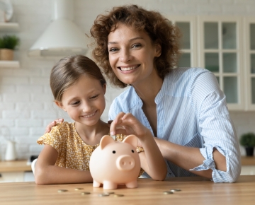 Mother and daughter putting money in piggy bank