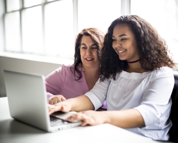 mother and daughter looking at laptop with window in background