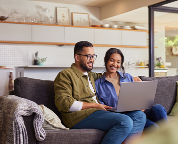 couple sitting on couch looking at laptop