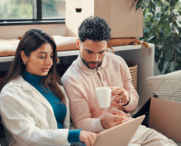 couple sitting on couch looking at laptop and drinking coffee