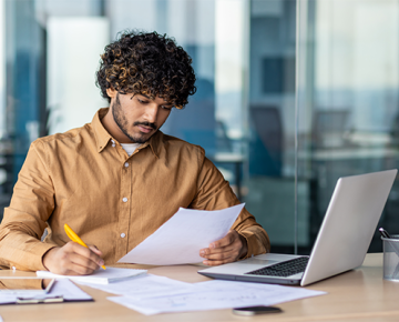 man in office looking at papers and laptop and writing