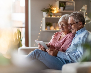 elderly couple sitting on couch looking at tablet