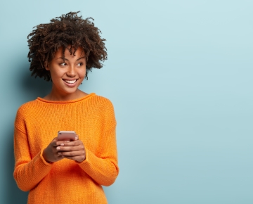 woman on phone in orange sweater with blue background
