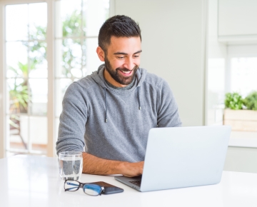 man in bright room looking at laptop next to glass of water