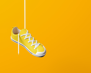 yellow shoe hanging from shoestring against yellow background