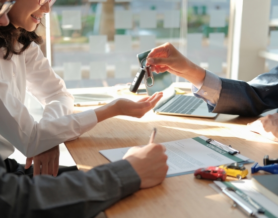 Person handing keys to another person with a contract. 