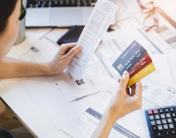 Person holding 3 credit cards with documents and a calculator. 