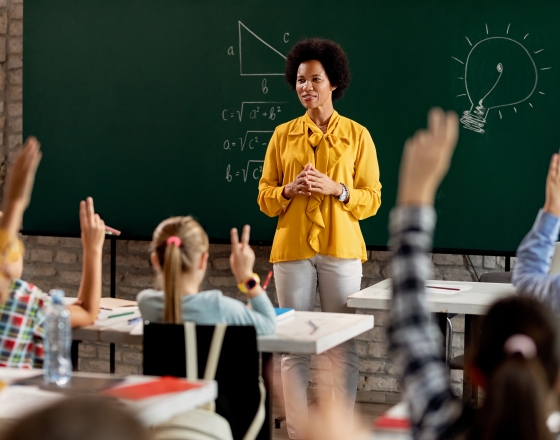 teacher wearing yellow and students raising their hands